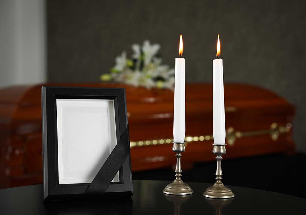 Lit candles, empty frame, and a casket in background.
