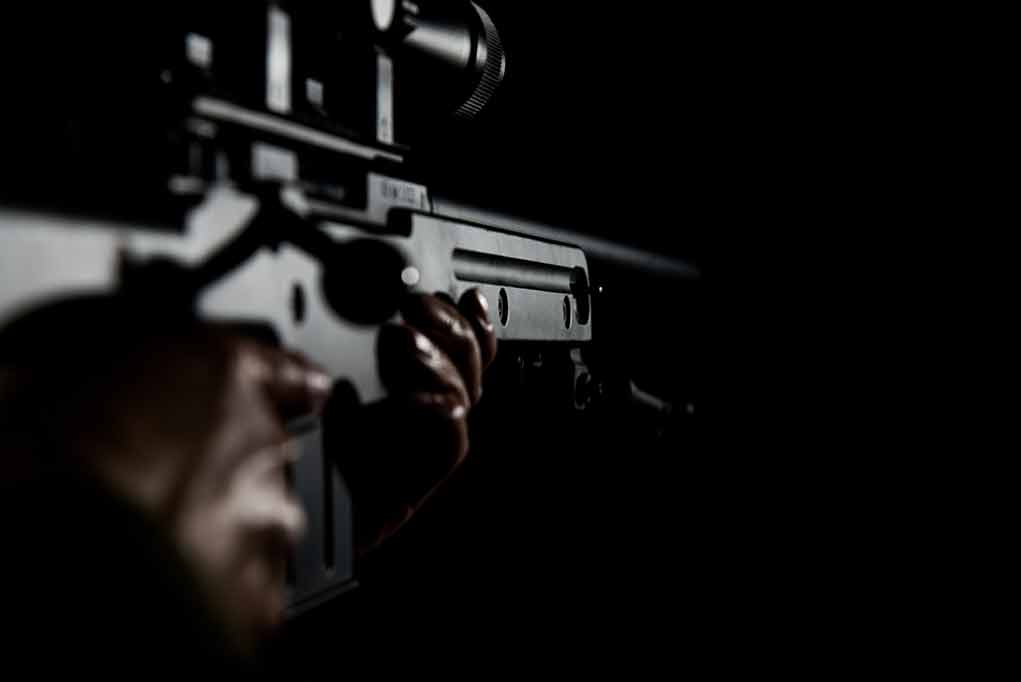 Person holding a rifle in dark surroundings.