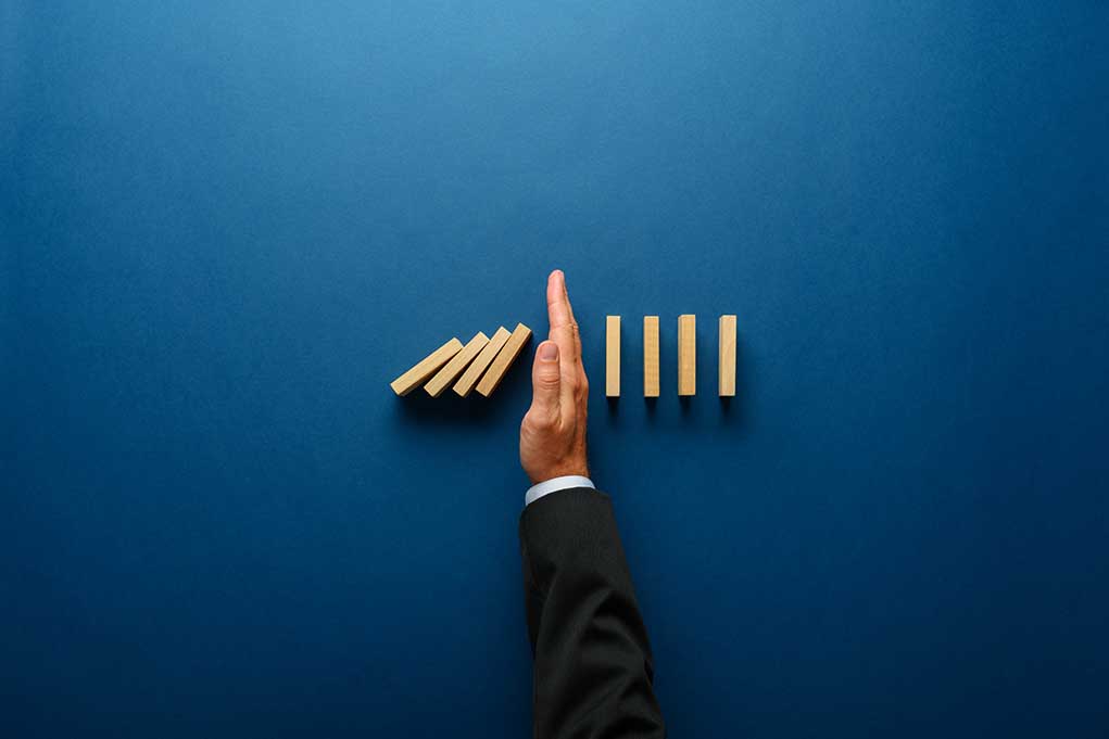 Hand stopping dominoes from falling on blue background.