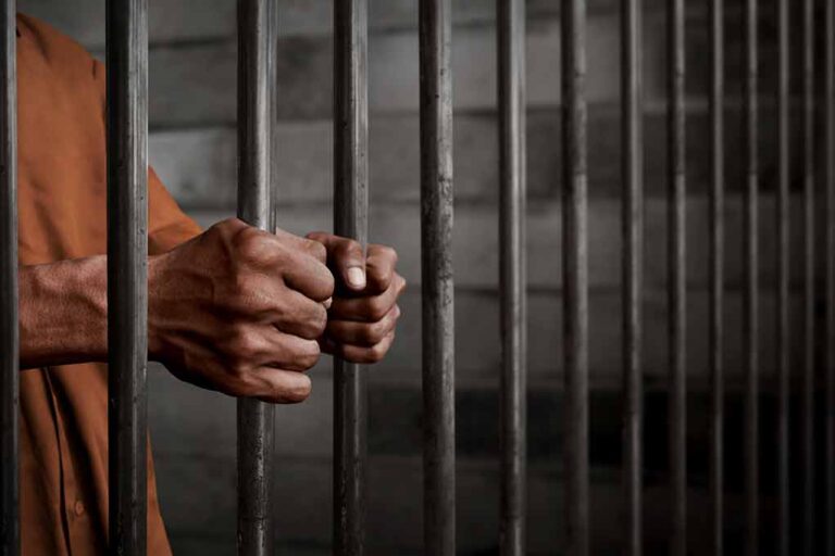 Hands gripping prison bars in a jail cell.