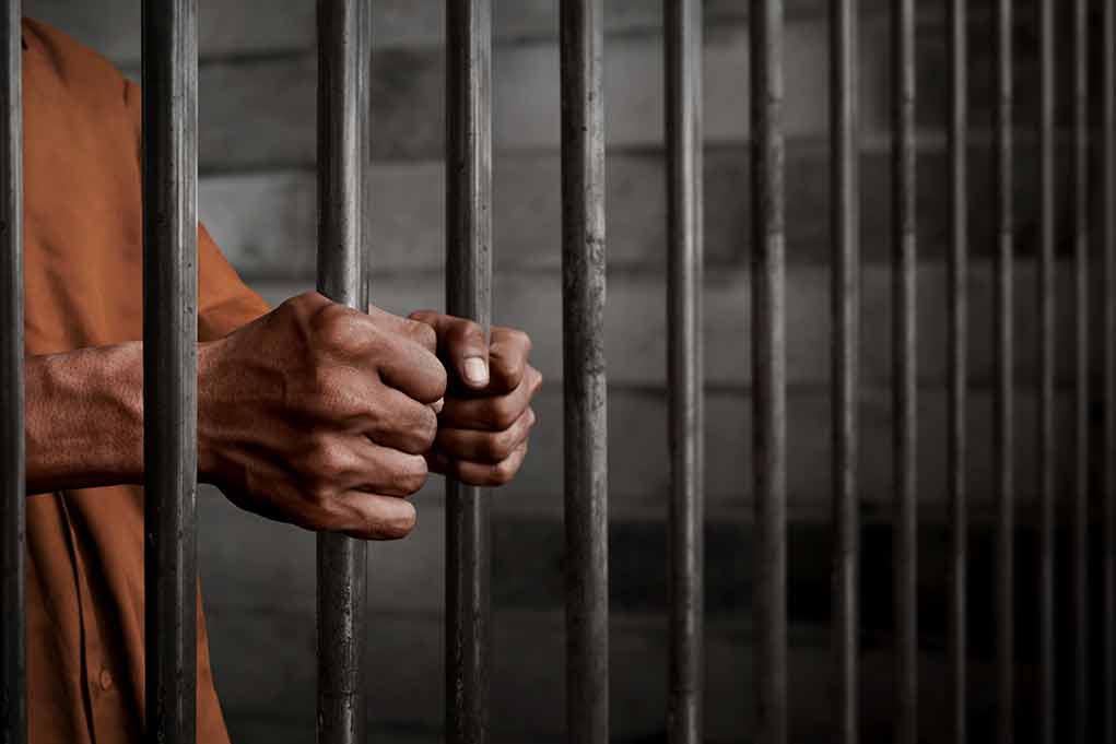 Hands gripping prison bars in a jail cell.