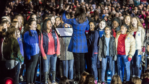 Group of people singing under conductor’s direction at event.
