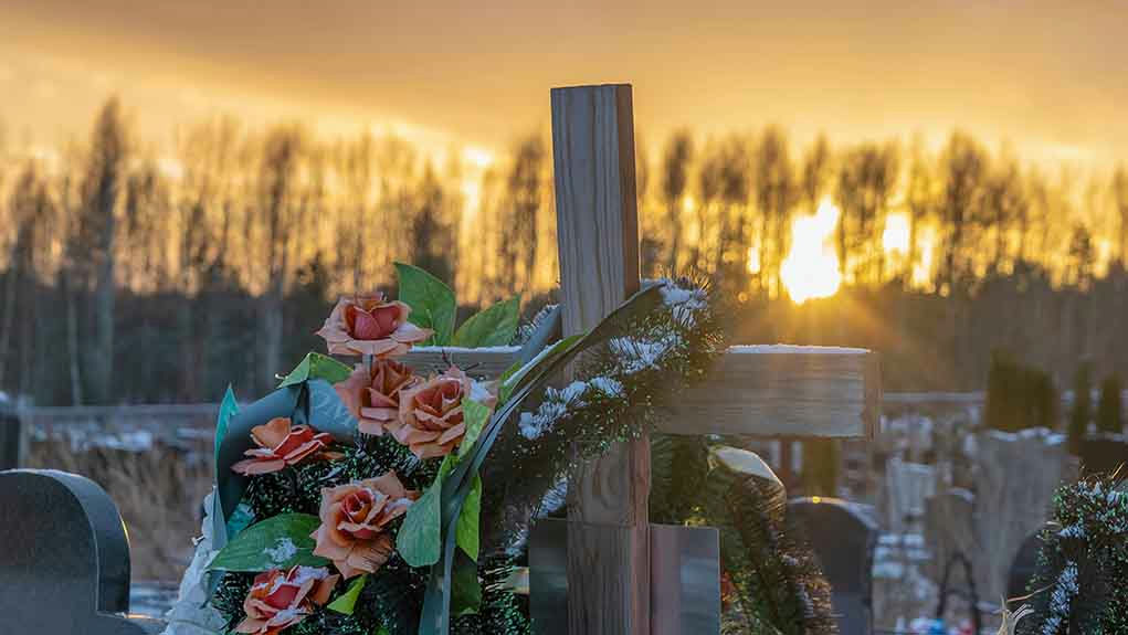 Wooden cross with flowers at sunset in a cemetery.