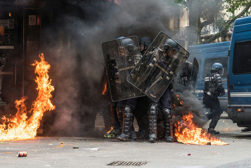 Riot police in protective gear amidst fire and smoke.
