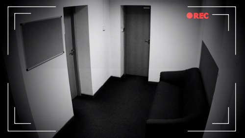 CCTV footage of an empty hallway with doors and sofa.