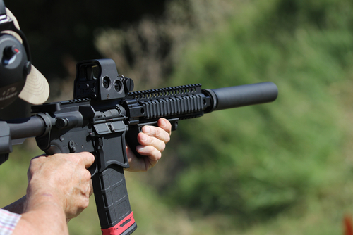 Person aiming AR-15 rifle outdoors.