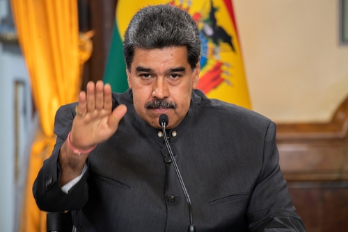 A political leader gesturing during a press conference with a Venezuelan flag in the background