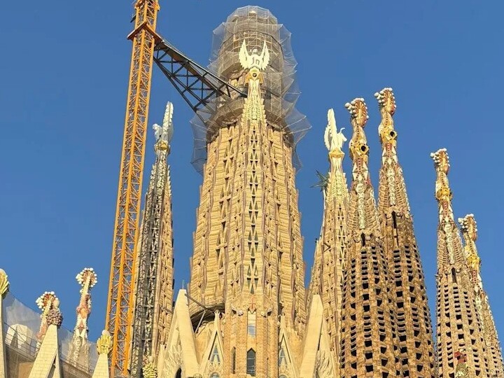 Construction view of the Sagrada Familia with cranes and intricate towers against a blue sky