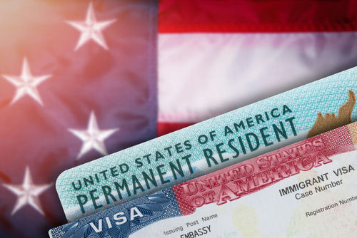 Green card and visa with U.S. flag background.